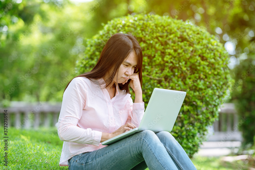Asian woman sitting green park using laptop computer. Woman working on laptop happy entrepreneur business using notebook with hands typing on keyboard home office during coronavirus quarantine period Asian woman sitting green park using laptop computer. Woman working on laptop happy entrepreneur business using notebook with hands typing on keyboard home office during coronavirus quarantine period