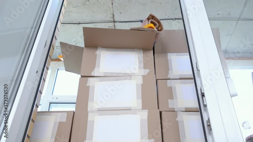 Mountain of cardboard boxes with labels for text is lined as wall on balcony, standing and dangerously swaying. Things for the move, problem of storage in small apartment photo