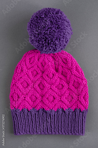 Beautiful two color handknitted hat with pompon on gray background. Top view