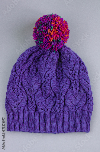 Beautiful kace handknitted hat with multicolored pompon on gray background. Top view