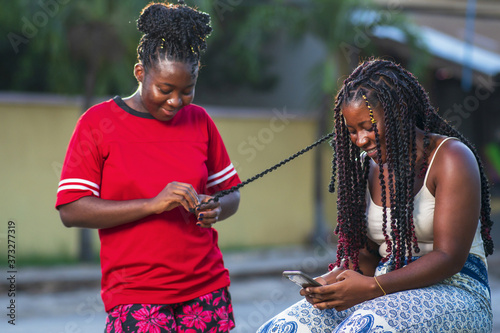 Canvas Print Two African American female friends smiling and braiding hair outdoors