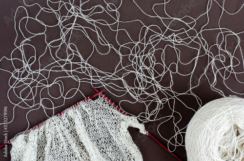 handknitted scarf of lace wool yarn on wood knitting needles and white yarn ball. dark background, top view