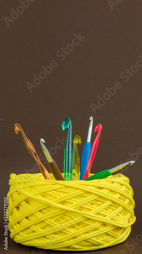 t-shirt yarn ball yellow color with colorfull crochet hooks on brown background. Handmade craft recycle eco concept