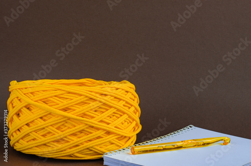 orange t-shirt yarn ball and orange crochet hook on notebook on brown background. Craft, handmade, hobby concept.