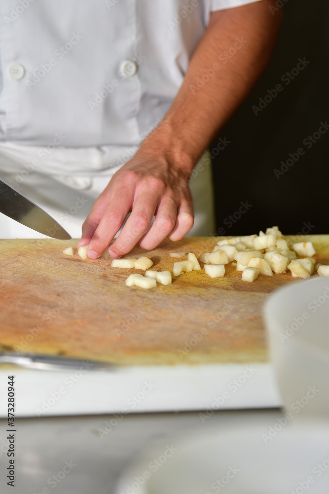 Male chef cutting potatoes with a kitchen knife on a cutting board on an out of focus background. Cooking concept.