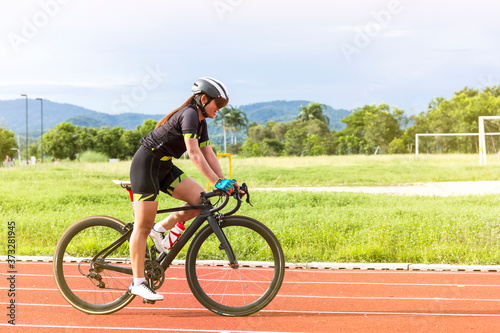 asian young woman athletes cycling on a race track intently and happily at outdoor sports field in bright day