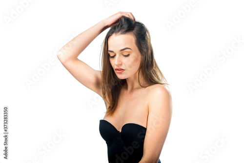 Portrait of charming beautiful woman in deep neckline dress. Girl with closed eyes holds hand near head. White background. Pretty female with closed eyes in black lingerie.