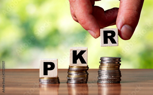 PKR Pakistan currency word symbol - business concept. Hands put wooden block on stacked increasing coin.