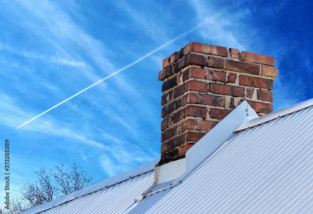 Old brick chimney on blue sky background with plane streak