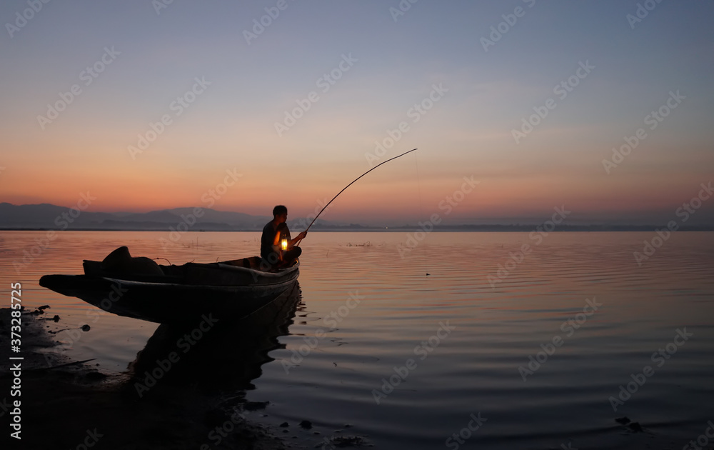 At lake side, asian fisherman sitting on boat and using fishing rod to catch fish at the sunrise