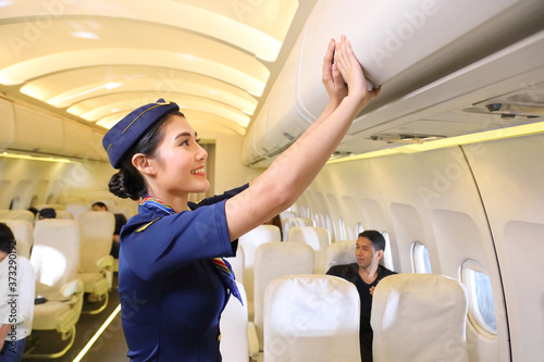 Female flight attendant closing the overhead luggage compartment lid after all passengers are seated and prepare to take off