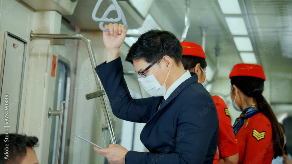 Asian businessman wear mask while traveling to work on skytrain. Prevent Coronavirus, bacteria in public place from people. Business people use tablet outside meeting at peak hour no social distancing Asian businessman wear mask while traveling to work on skytrain. Prevent Coronavirus, bacteria in public place from people. Business people use tablet outside meeting at peak hour no social distancing