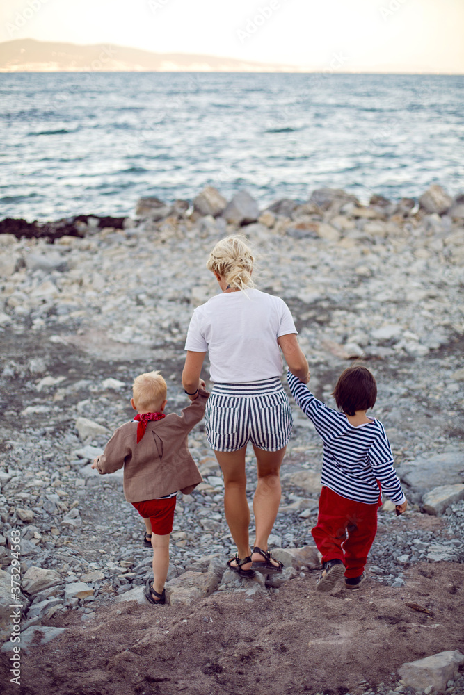 mom walks with her back with two sons walks along the pebble embankment mom walks with her back with two sons walks along the pebble embankment