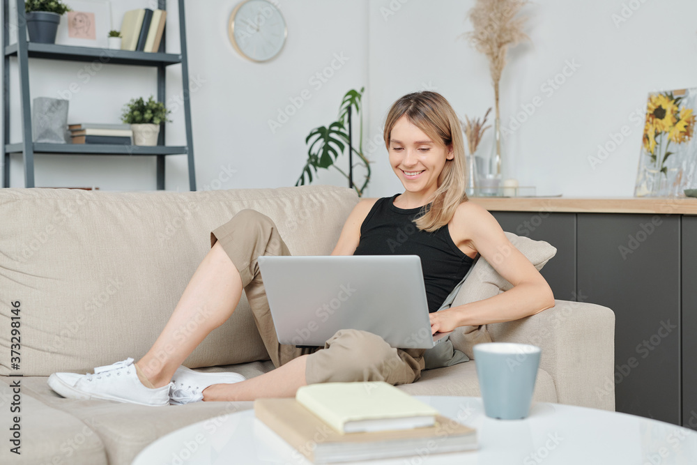Young cheerful blond woman looking at laptop display while watching online movie Young cheerful blond woman looking at laptop display while watching online movie