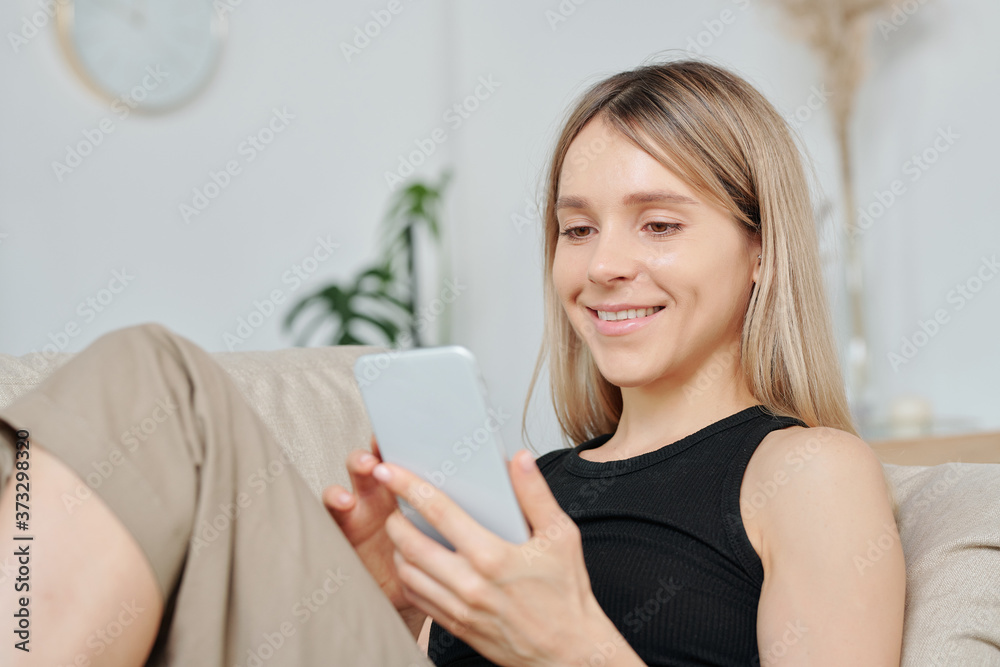 Young smiling blond female in black vest relaxing with smartphone at leisure Young smiling blond female in black vest relaxing with smartphone at leisure