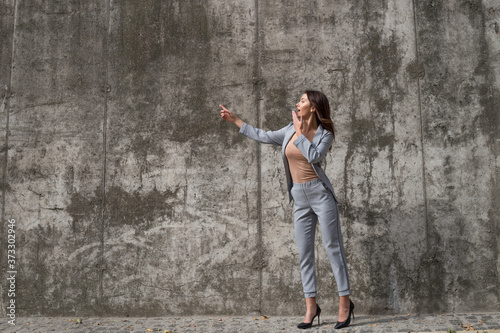 Take a look  Full length of beautiful young woman pointing away with smile while standing against concrete background 