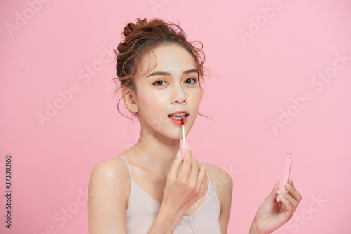 Beautiful young Asian woman applying lipstick isolated over pink background.