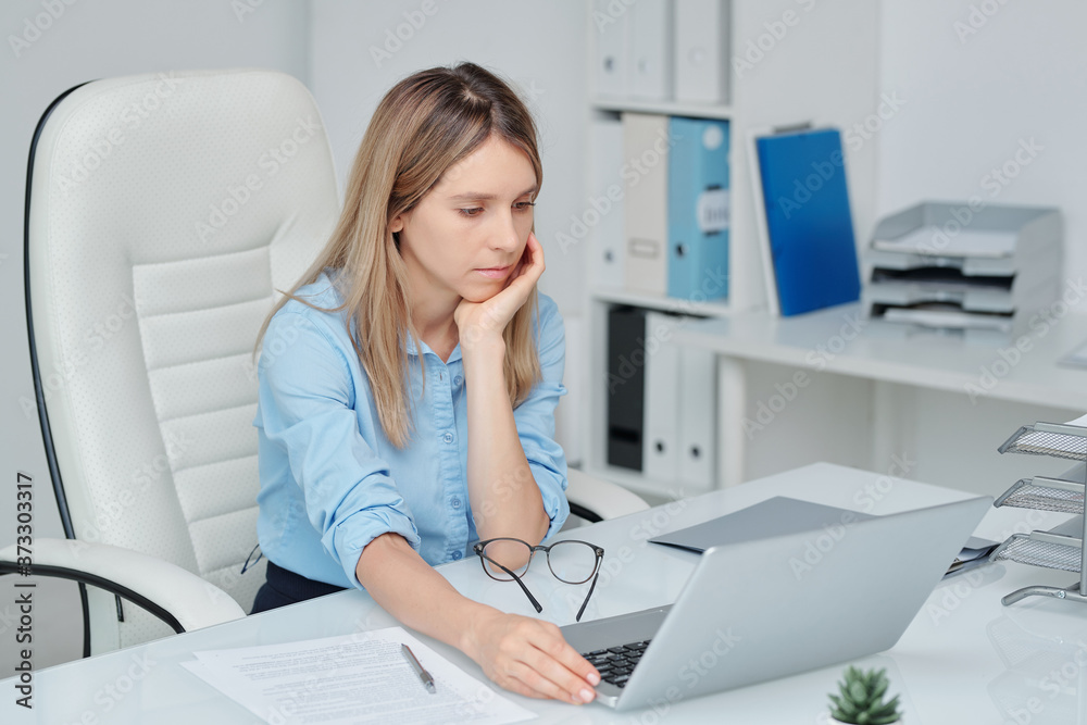 Young sad and tired female broker in smart casualwear looking through data Young sad and tired female broker in smart casualwear looking through data