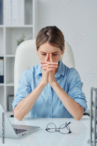 Young tense businesswoman keeping her hands by face while trying to concentrate