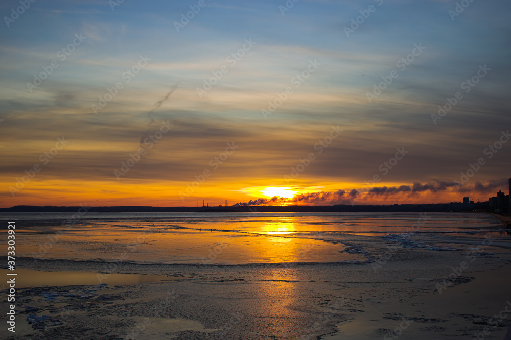 Frosty bright sunset over the freezing Volga river. View from the water to the sunset and the silhouette of an oil refinery. Frosty bright sunset over the freezing Volga river. View from the water to the sunset and the silhouette of an oil refinery.