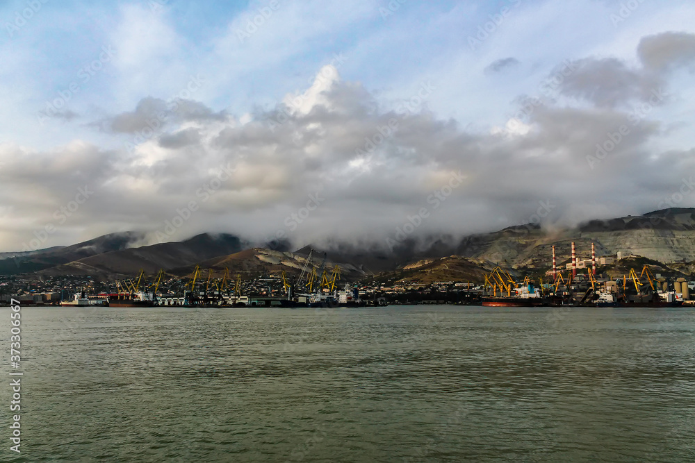 The seaport on the background of mountains during cloudy, cloudy weather in the mountains. Moored for unloading / loading sea ships against the background of mountains in the clouds.
