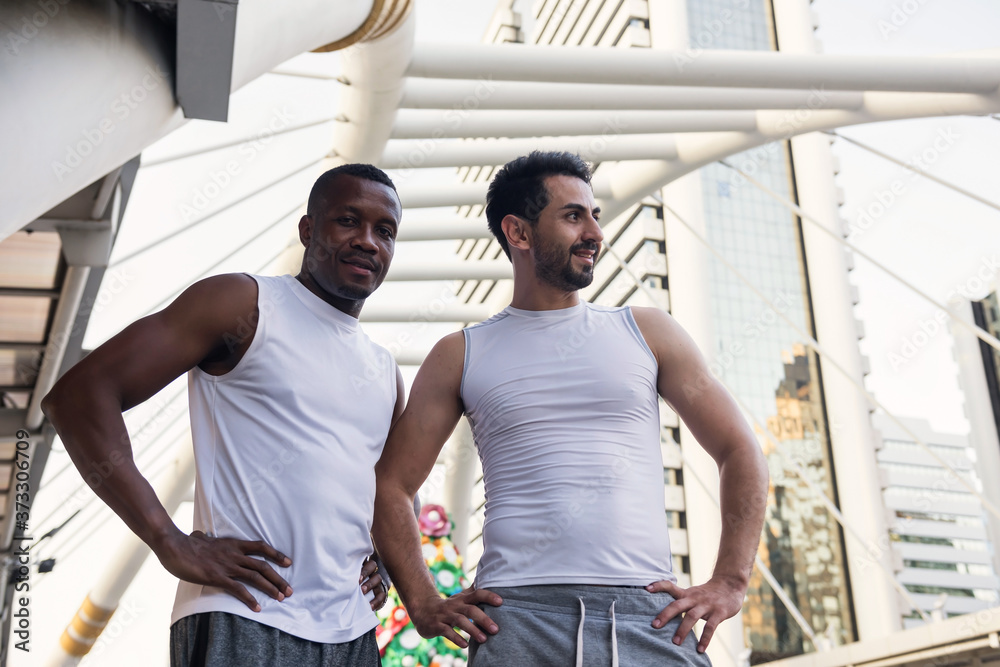 Portrait of young American and black African friends relax after running exercise in city. Modern urban downtown skyline background. Sport and healthy lifestyle in town. black lives matter