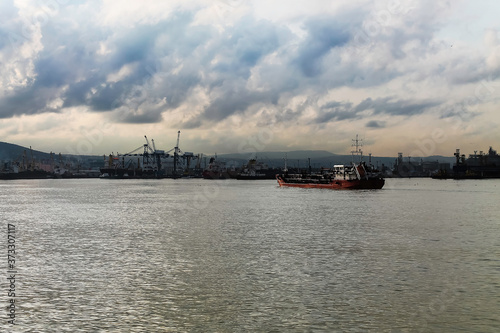 A red cargo ship for the transportation of liquefied gas along rivers and seas enters the port. Cloudy weather in the middle of autumn on the seaside. 