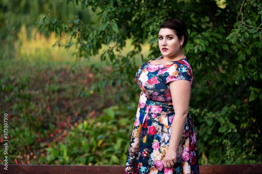 Plus size fashion model in floral dress outdoors, beautiful fat woman with big breasts in nature