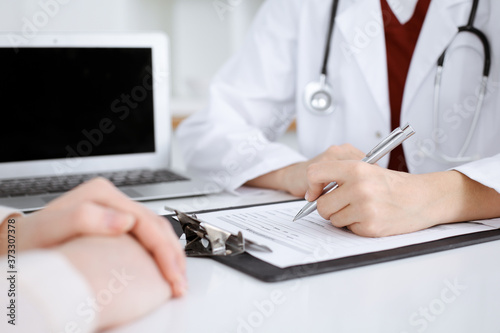Unknown woman-doctor filling up an application form while consulting patient. Medicine concept