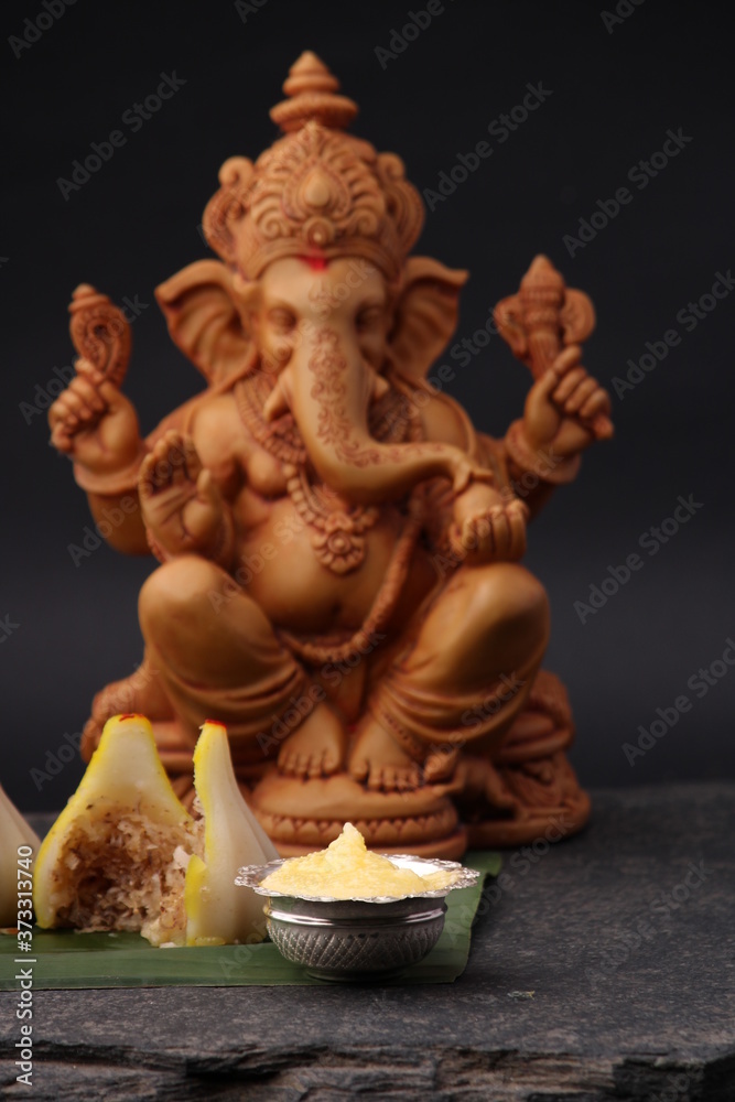 Modak- a traditional dish made on Ganpati festival in India. served with clarified butter. Ganesh idol at background