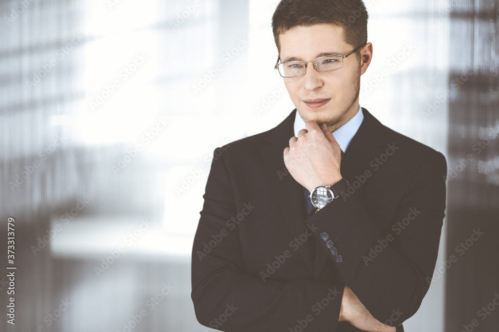 Young businessman wearing suit, with glasses, while standing in the office. Business success concept nowadays Young businessman wearing suit, with glasses, while standing in the office. Business success concept nowadays
