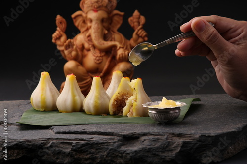 Modak- a traditional dish made on Ganpati festival in India. served with clarified butter. Ganesh idol at background photo