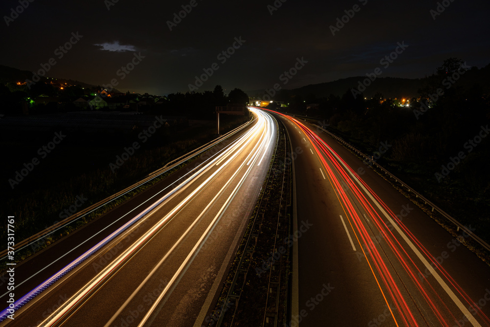 Highway in night with light rails of cars and trucks