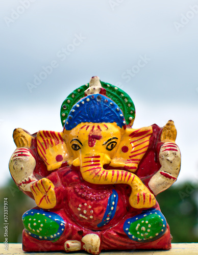 Wooden colourful miniature lord ganesha idol with blurred sky and tree background