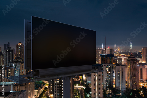 Blank black road billboard with KL cityscape background at night time. Street advertising poster, mock up, 3D rendering. Side view. The concept of marketing communication to promote or sell idea.