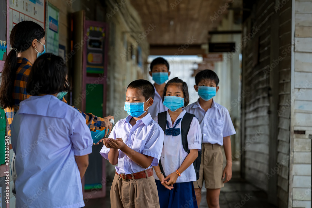 Fototapeta premium Teacher and elementary children with face mask are disinfecting hands at school after covid-19 quarantine and lockdown.