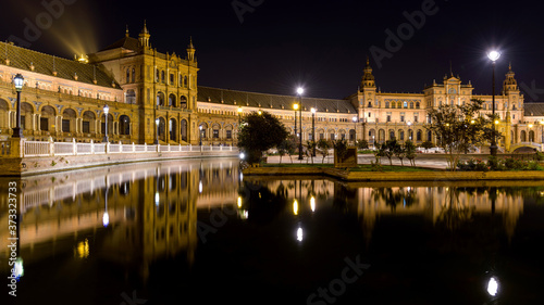 Spanish Square - A panoramic night view of illuminated semi-circular brick building of Spanish Square - Plaza de España, reflecting in its miniature canal. Seville, Andalusia, Spain.