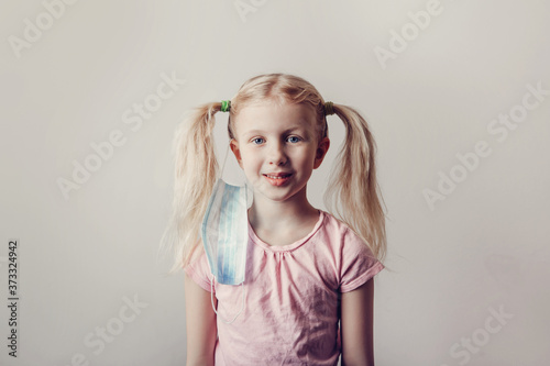 Portrait of Caucasian blonde girl taking off sanitary face mask. Preschool child with protective mask on ear. End finish of covid-19 quarantine and self isolation concept.
