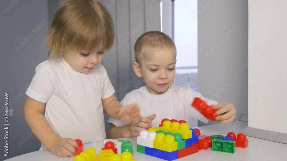 Happy children at home at the table build a house of colored cubes. Happy children at home at the table build a house of colored cubes.
