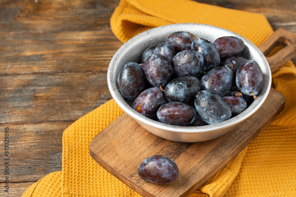 Ripe plum. Lots of plums in a metal bowl on a brown wooden table. Blue plums in a bowl close-up. Healthy fruits Ripe plum. Lots of plums in a metal bowl on a brown wooden table. Blue plums in a bowl close-up. Healthy fruits