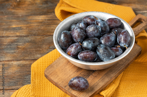 Ripe plum. Lots of plums in a metal bowl on a brown wooden table. Blue plums in a bowl close-up. Healthy fruits