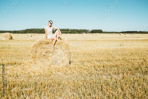 Wheat fields. Girl sitting on round ball of hay. Harvest, end of summer. 