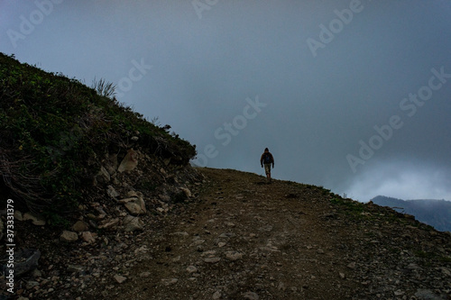 Man from the back with a backpack is trekking in the mountains in the fog