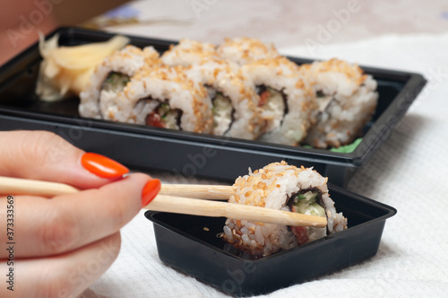 Woman eating delivered at home sushi from a container with japanese sticks.