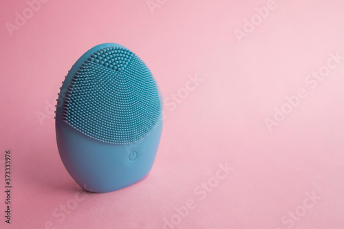 Blue facial cleansing brush on pink background. Beauty and skincare concept. Brush for face lifting, anti-aging wrinkles and massage