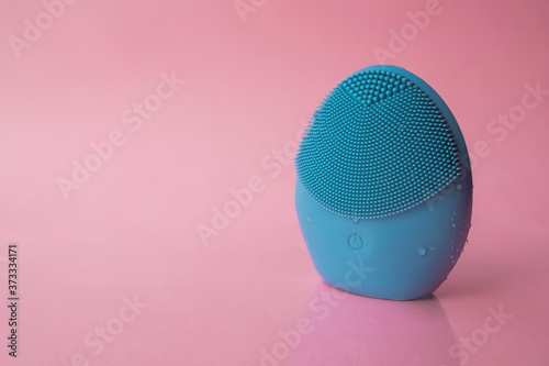 Blue facial cleansing brush on pink background. Beauty and skincare concept. Brush for face lifting, anti-aging wrinkles and massage
