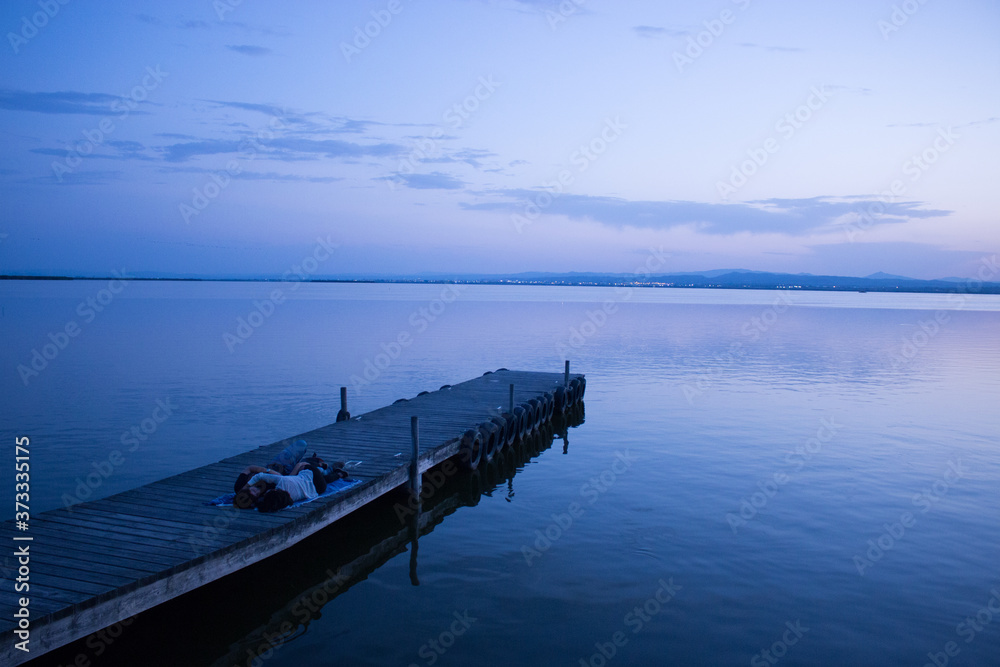 novios tumbados y abrazados en un embarcadero de la albufera (valencia) mientras disfrutan del precioso atardecer