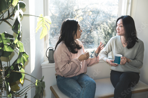 Foto A British-Bangladeshi woman and an Asian woman chat over a cup of tea while sitt