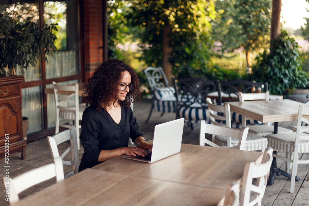 The beautiful young woman sitting at the table typing on the laptop at the terrace. The beautiful young woman sitting at the table typing on the laptop at the terrace.