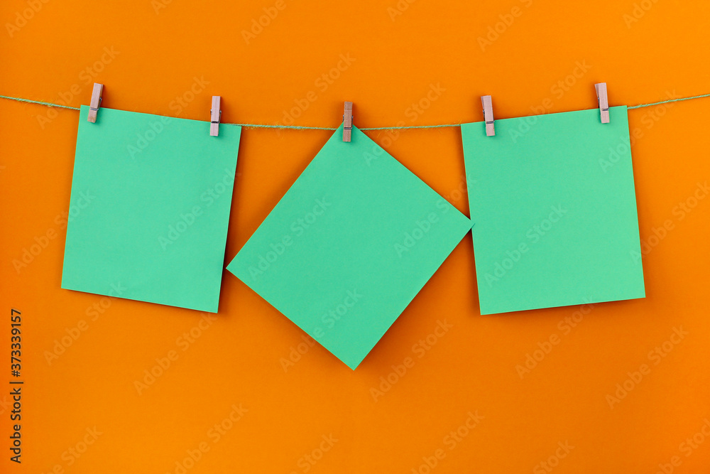 Three green blank sheets of paper hang from a rope against an orange background. Note paper. Reminder. Place for your text.
Three green blank sheets of paper hang from a rope against an orange background. Note paper. Reminder. Place for your text.